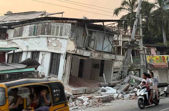 A family on a moped pass a building that's collapsed due to earthquake damage.